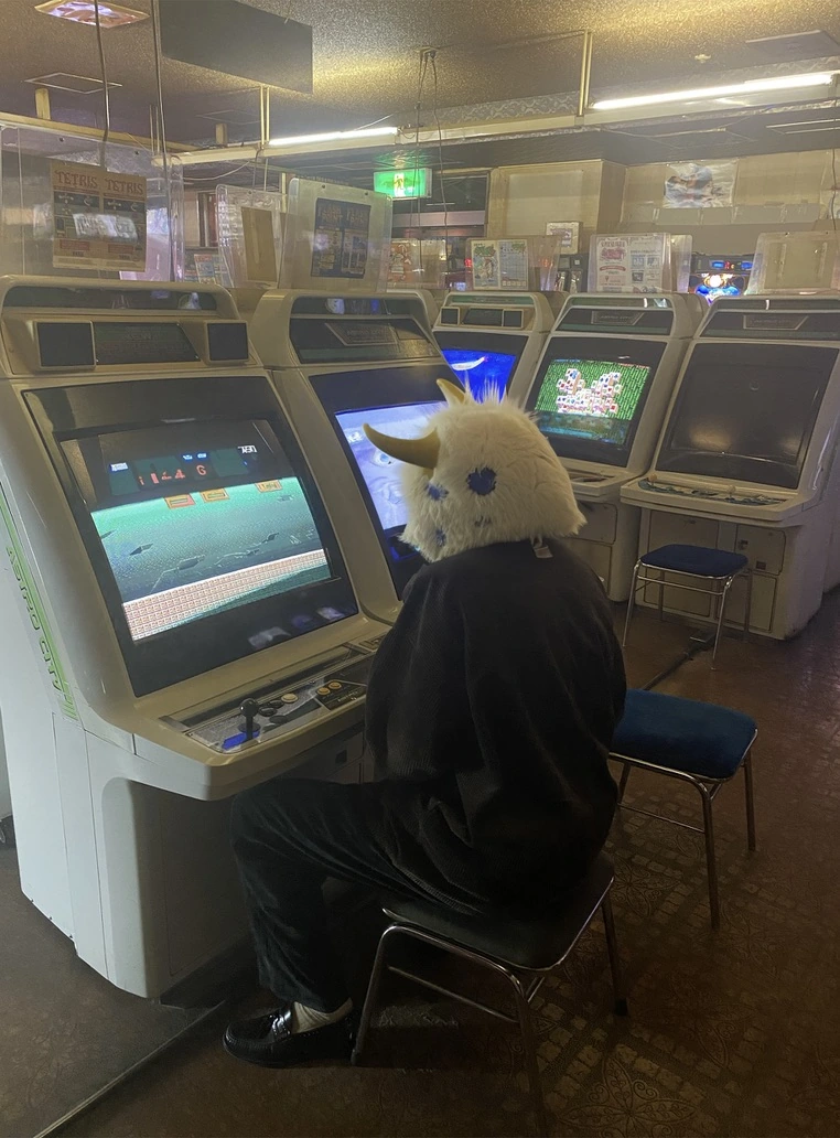 ゲーム機の前に座る、白い角のある仮面を身につけた人物